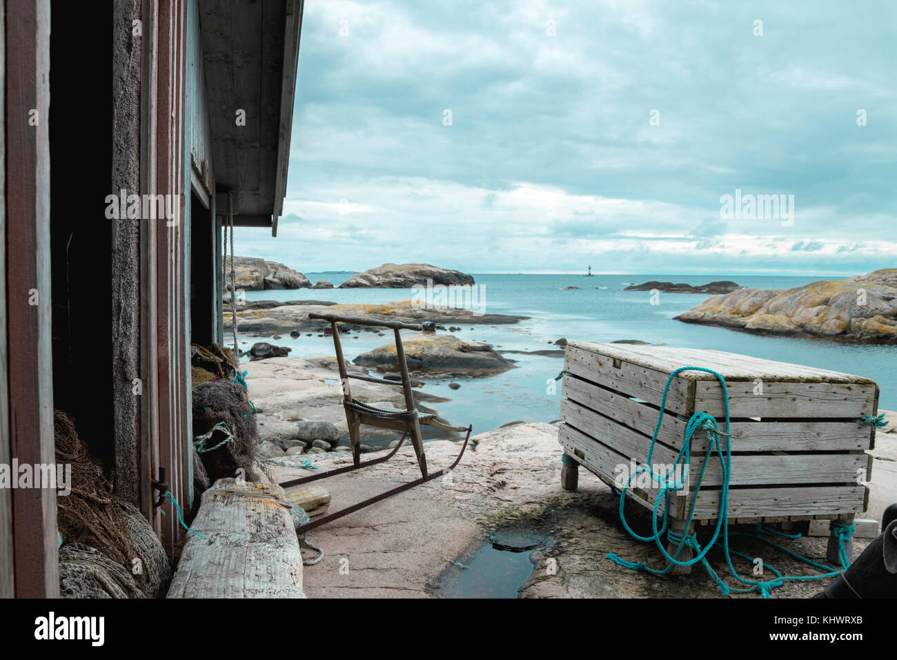 Isresting la trottinette des neiges scandinaves antiques dans la solitude à l'extérieur d'un bateau en bois flotté rustique maison entourée par l'océan bleu turquiose et pierre de granit gris Banque D'Images