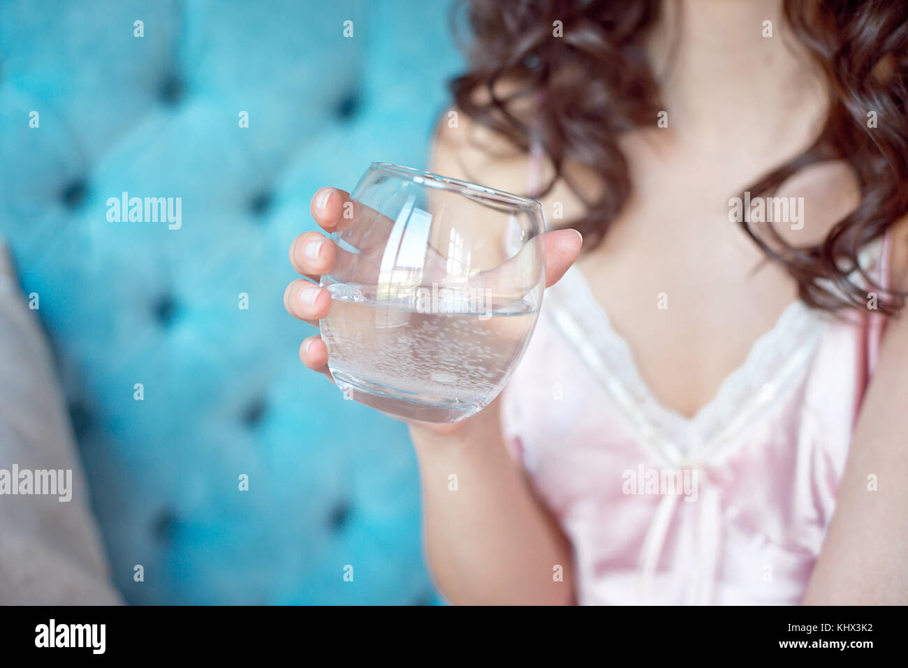 Cie jolie femme avec les yeux baissés de porter l'ombre d'oeil tenant un verre de boisson fraîche dans sa main qu'elle siège en souriant sur un canapé à la maison avec un s Banque D'Images