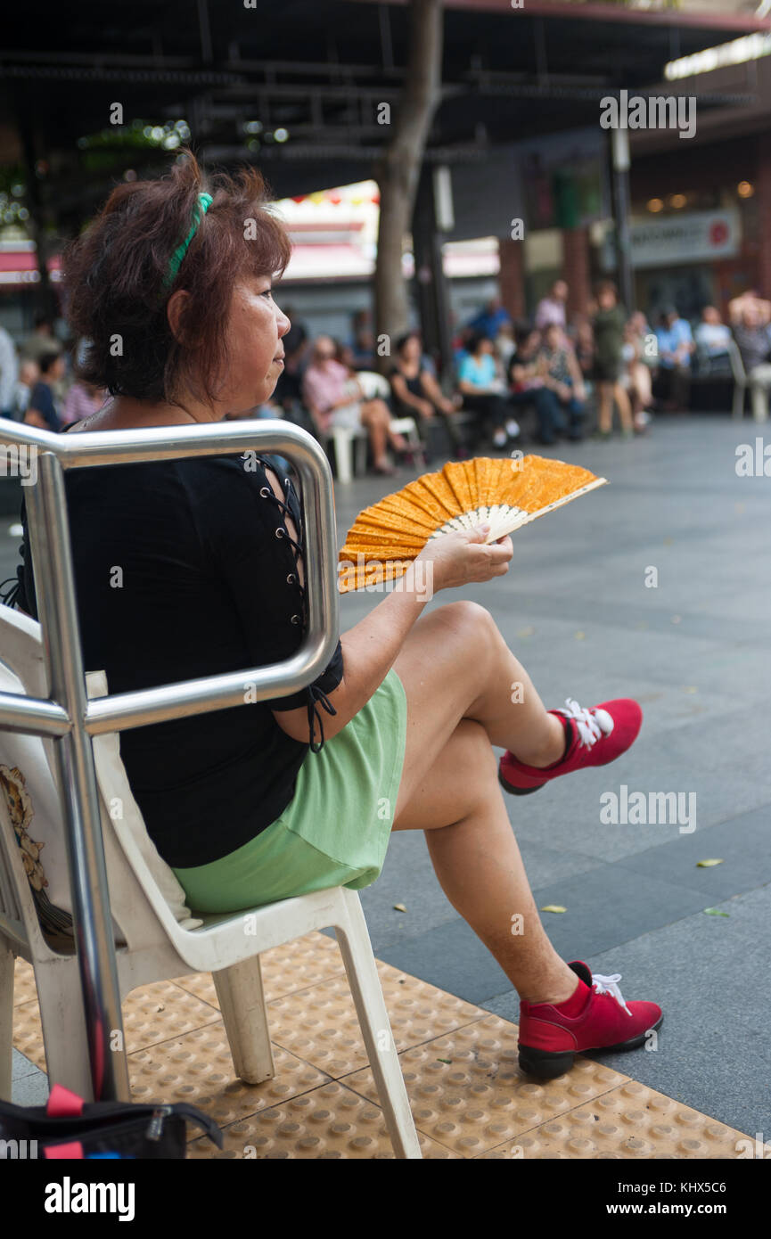 22.10.2017, Singapour, République de Singapour, en Asie - une femme est vu fanning elle-même avec un ventilateur alors qu'elle voit un groupe de personnes âgées effectuer un lin Banque D'Images