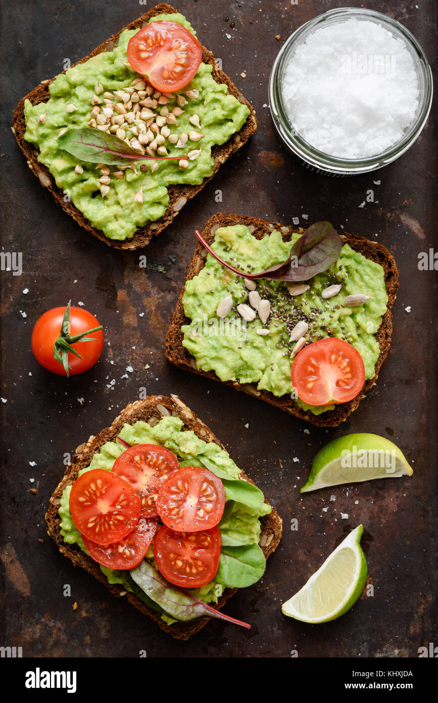 Toasts à l'avocat utile avec les germes, graines de tomate, sel de mer et de flocons. Vue de dessus de table, vertical Banque D'Images