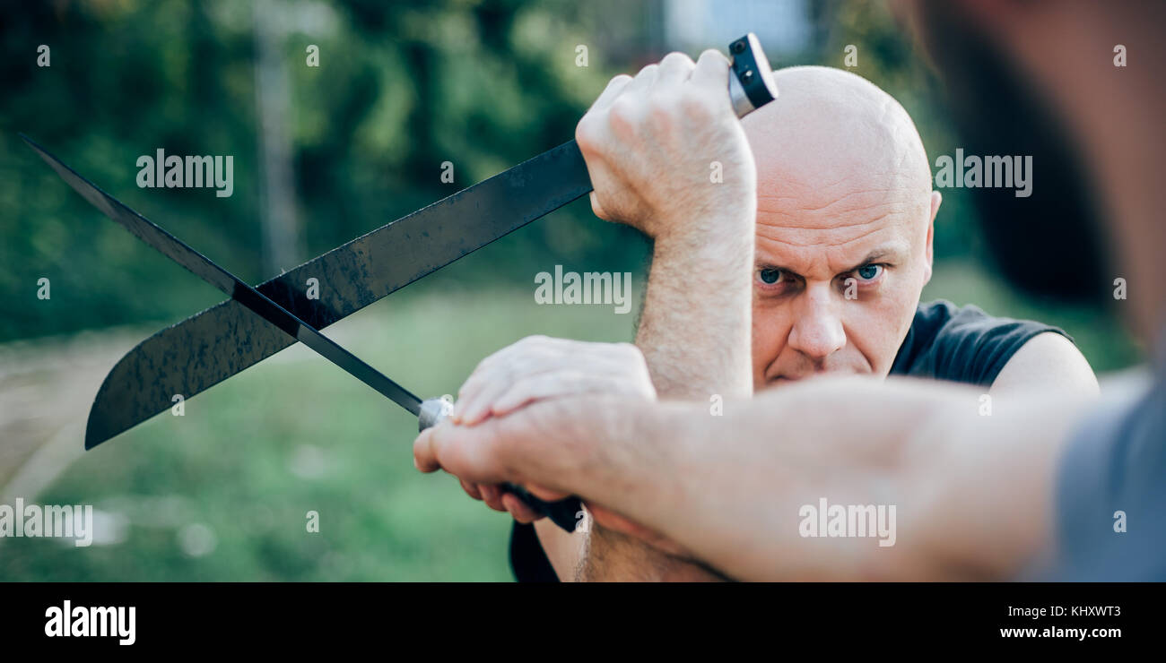 Un instructeur d'arts martiaux démontre le concept de combat de machettes.Formation d'armes à long couteau.Démonstration avec une vraie machette métallique Banque D'Images
