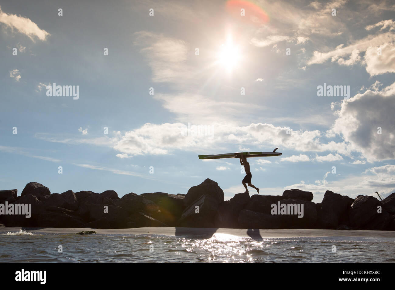 Jeune homme marchant sur les rochers, faisant de surf Banque D'Images