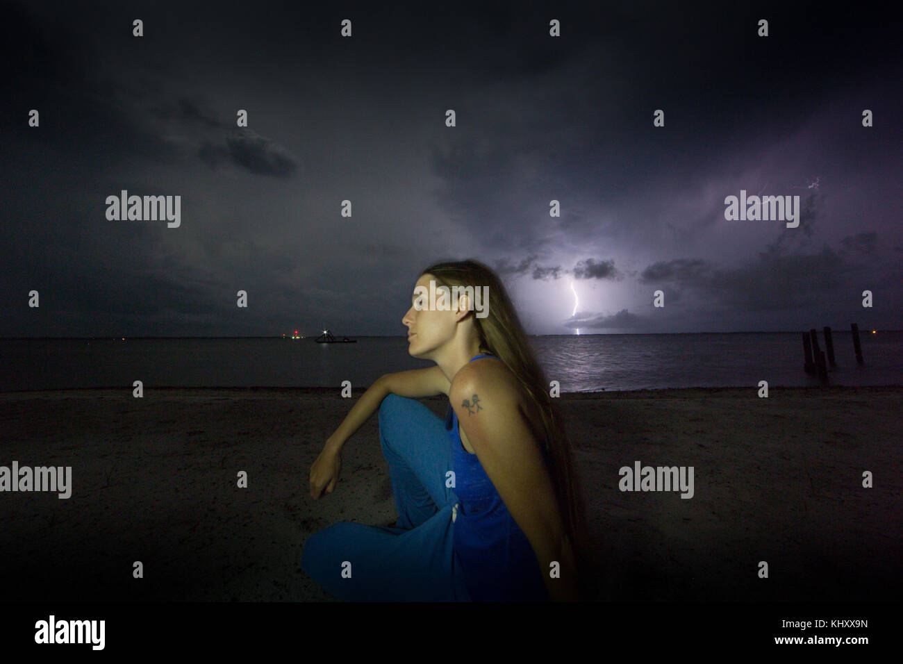 Femme assise sur la plage la nuit, la foudre dans le ciel en arrière-plan Banque D'Images