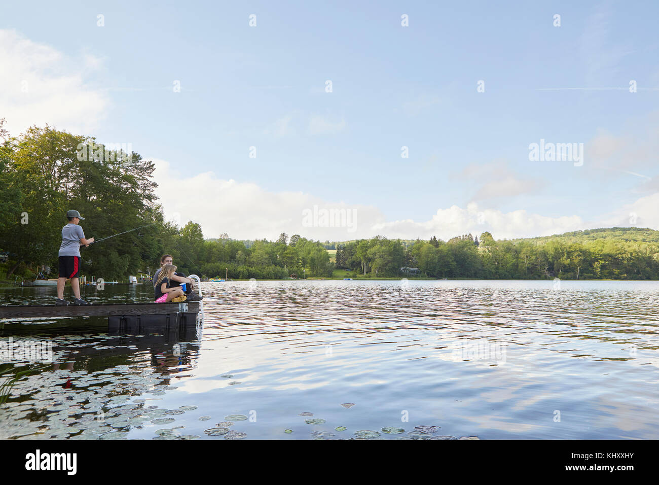 Trois enfants sur la jetée à côté lac, jeune garçon à l'aide de pêche canne à pêche Banque D'Images