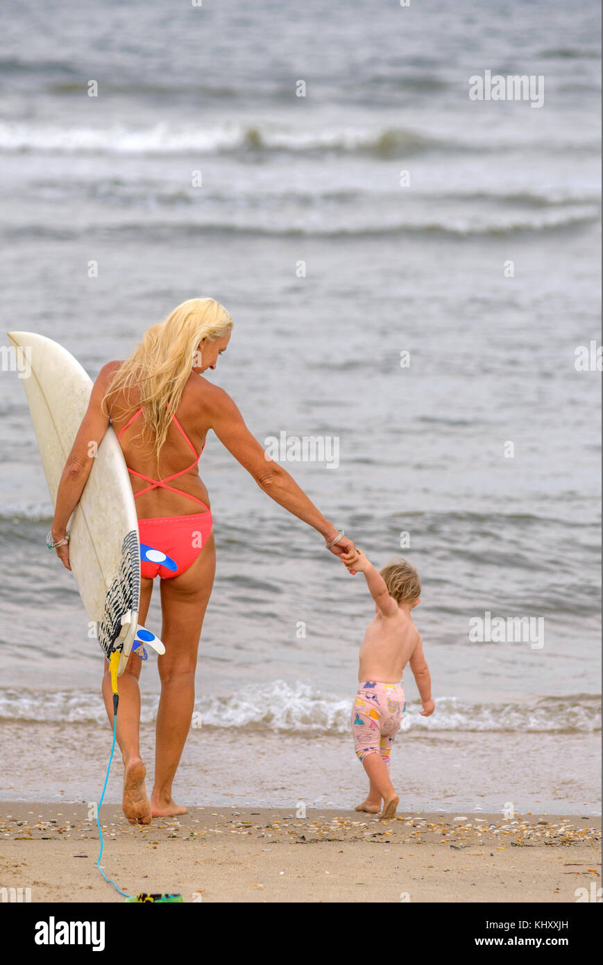 Vue arrière du surfeur femme au bord de l'eau avec tout-petit fille, Asbury Park, New Jersey, USA Banque D'Images