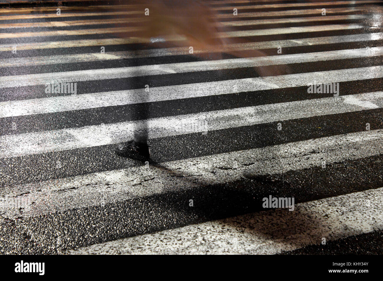 Rue ville pluvieuse réflexions : une jeune femme fragile de disparaître en traversant la rue humide dans la nuit étincelante Banque D'Images