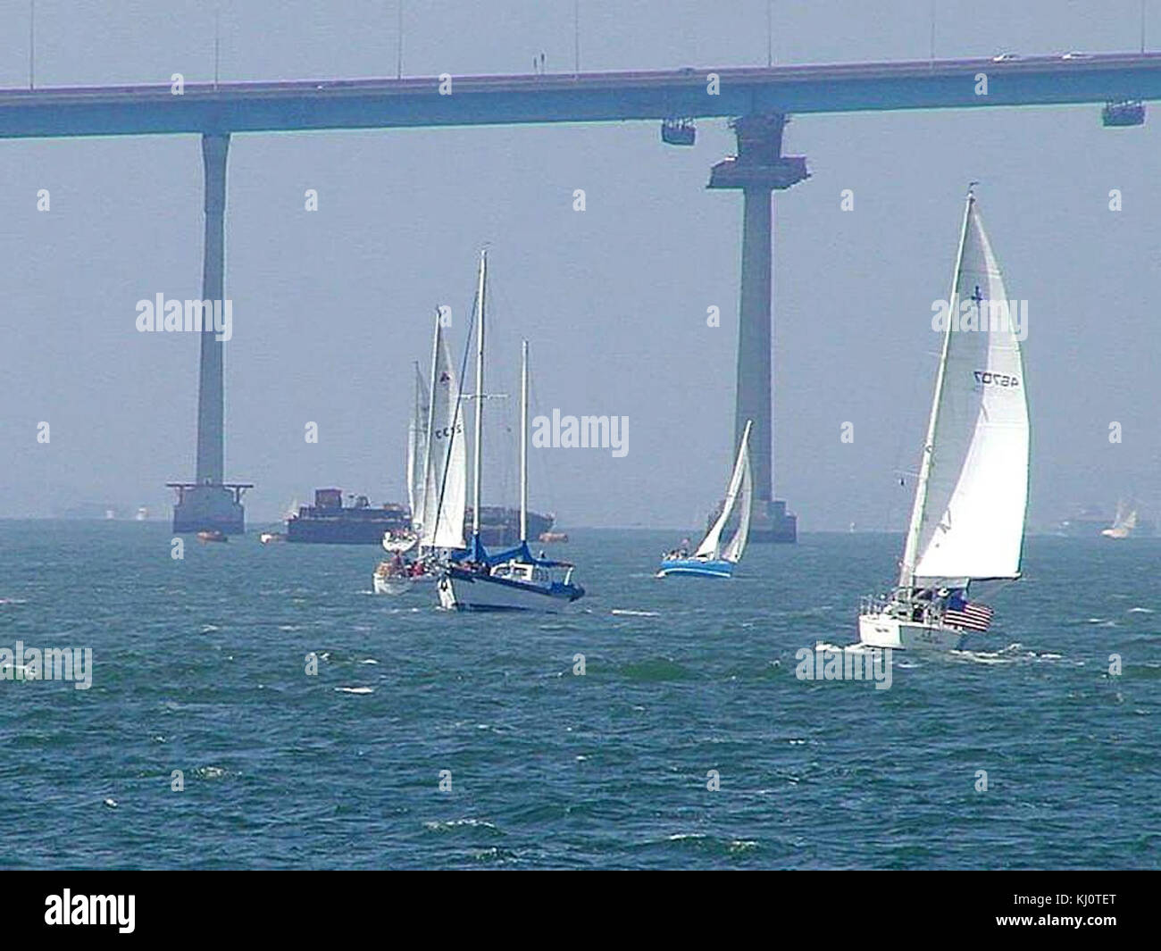Cette image montre l'emblématique Coronado Bridge à San Diego, avec des voiliers naviguant sur l'océan en dessous. La scène capture l'activité maritime dans la baie, avec des voiles qui bondissent dans le vent, créant une vue pittoresque sur la côte californienne. Banque D'Images