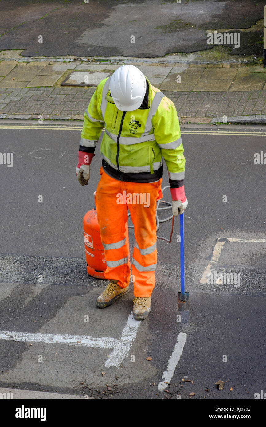 Travailleur homme portant des vêtements haute visibilité brûlant ancien marquage routier avec un lance-flammes england uk Banque D'Images