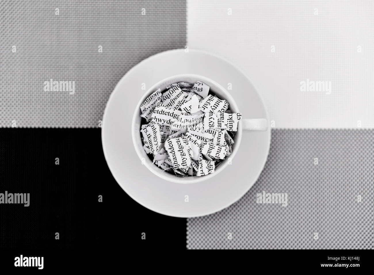Une lettre ou un document imprimé brisée en mille morceaux dans une tasse à café en céramique blanche placée sur un fond noir, fond blanc et gris Banque D'Images