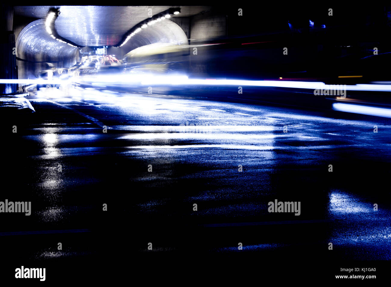 Le trafic de nuit floue des pluies sur les rues de la ville. voitures dans le motion blur roulant hors du tunnel à la légère des sentiers et des réflexions sur l'asphalte humide. Banque D'Images