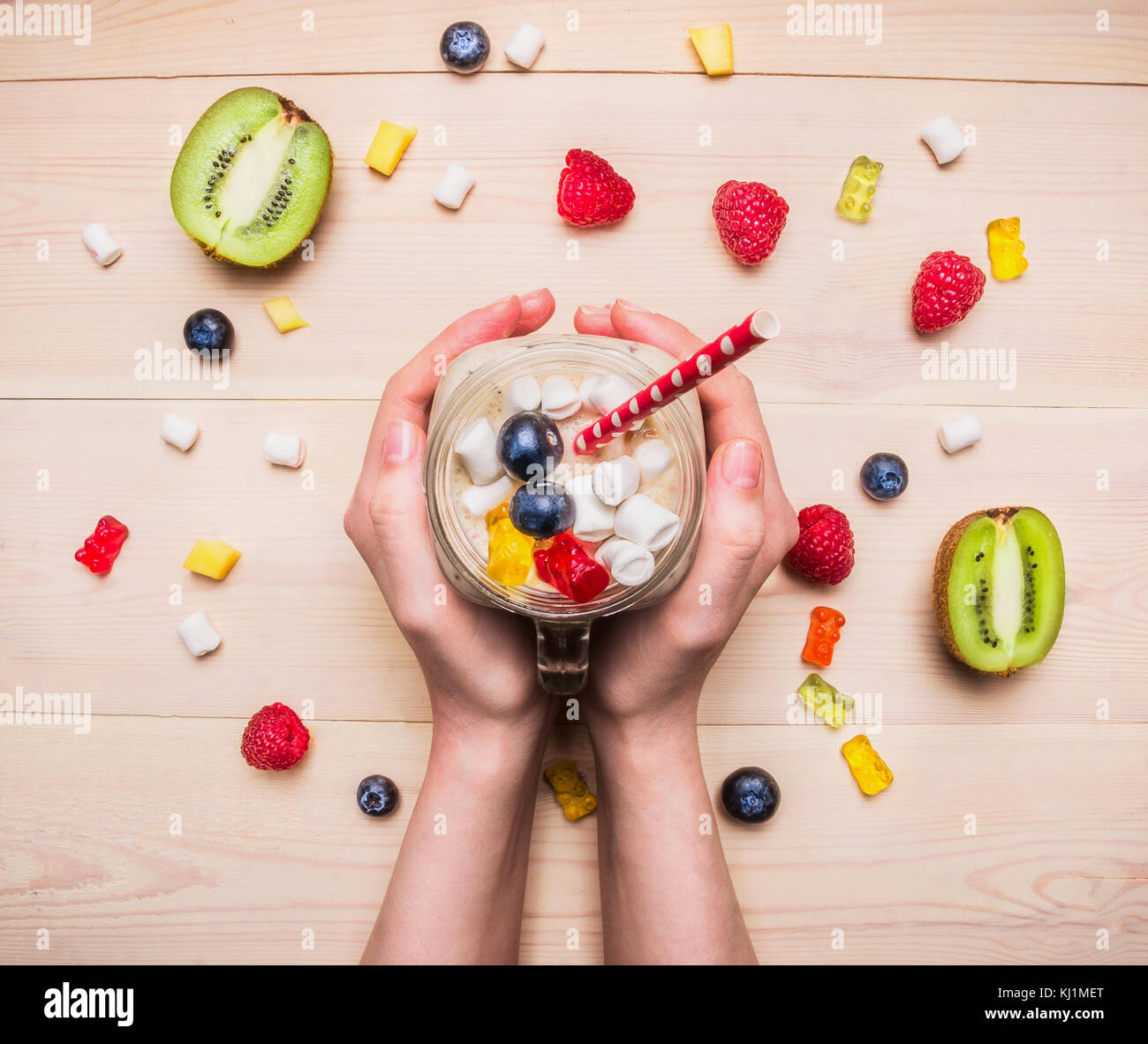 Girl holding un smoothie frais de framboise, de kiwi et bananes sur un fond de bois, avec réparties autour de la cœurs multicolores, petits fruits, gelée Banque D'Images