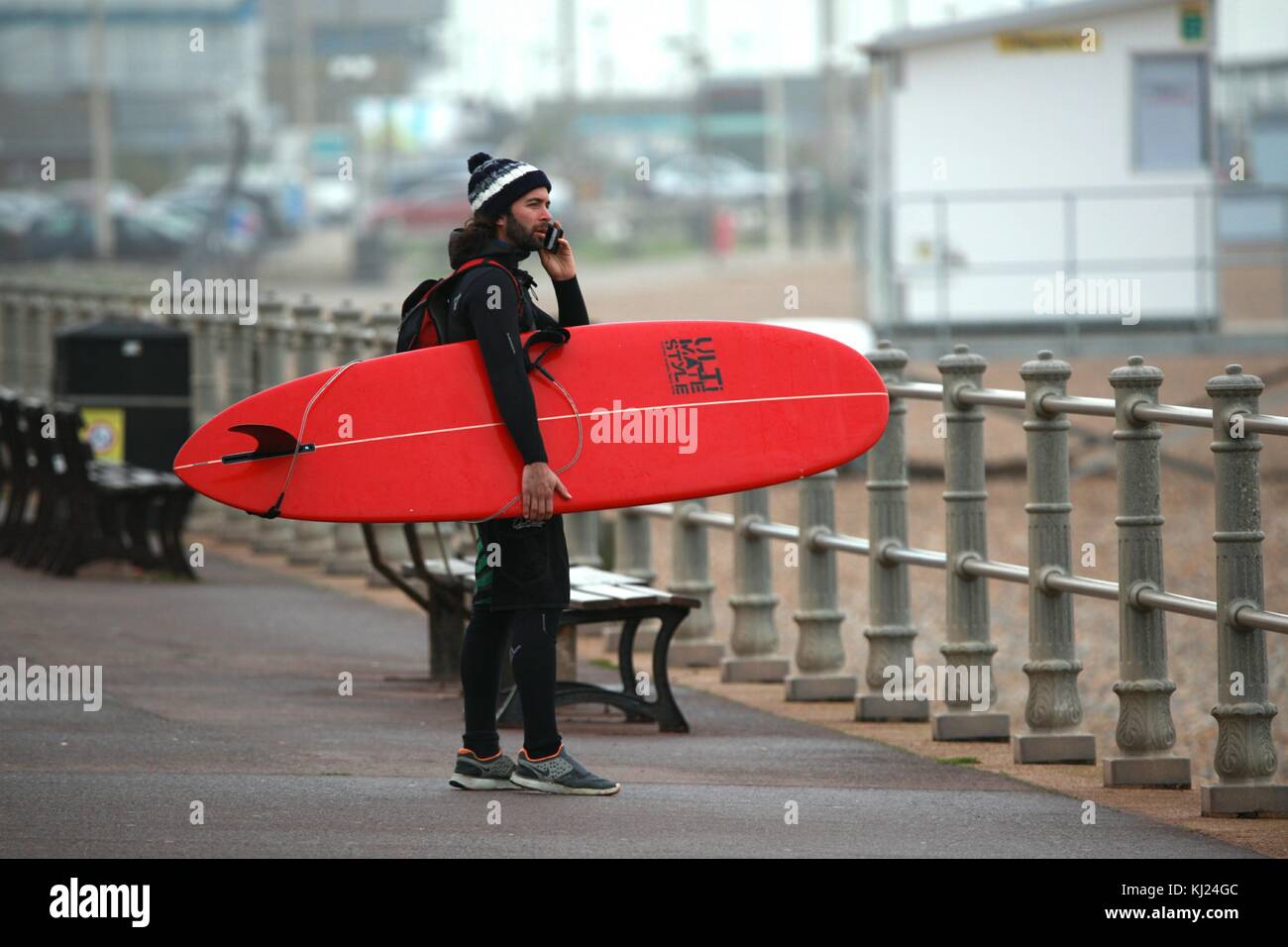 Hastings, East Sussex, UK. 21 novembre 2017. A man talking on a mobile phone transportant un surf sous le bras sur la promenade de front de mer de Hastings. Crédit photo : Paul Lawrenson /Alamy Live News Banque D'Images