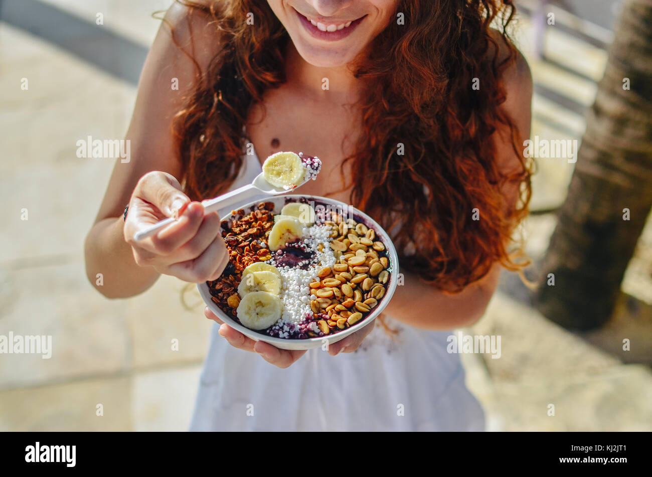 Young woman eating a l'açaï dans un bol, avec la banane, l'écrou et le tapioca. une nourriture typiquement tropical. Banque D'Images