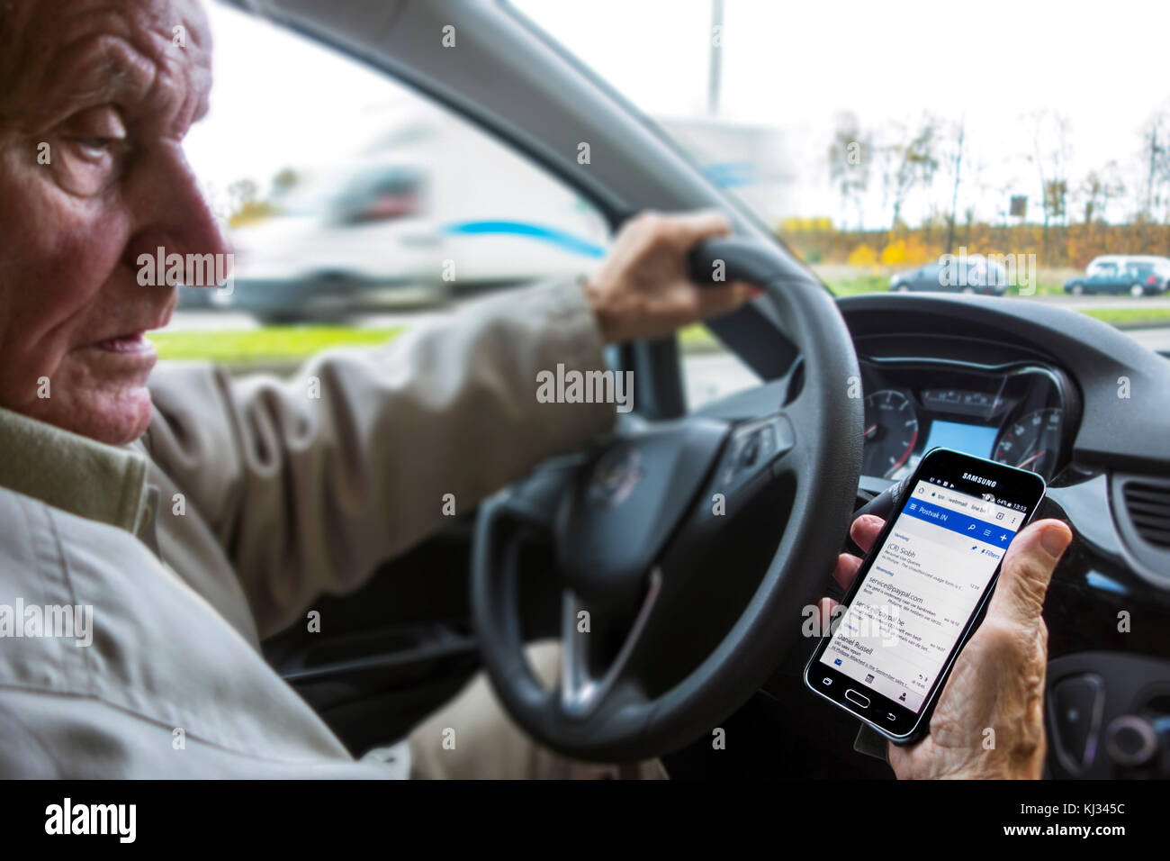 Vieil homme irresponsable au volant de la consultation des messages sur téléphone intelligent / smartphone / téléphone portable pendant la conduite automobile sur route Banque D'Images