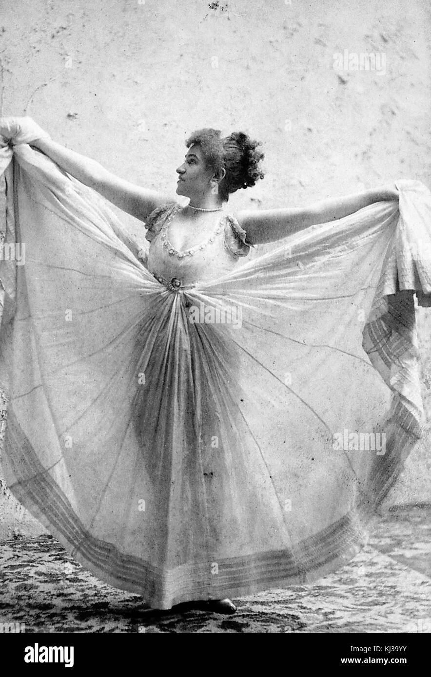 Portrait photographique de Minnie Renwood, elle tient les côtés de sa robe volumineuse à hauteur des épaules tandis que l'avant est encore suspendu au sol, elle était une danseuse populaire à New York dans les années 1890, elle a fait l'objet d'une affaire juridique importante qui a déterminé que les mouvements d'une danse ne pouvaient pas être protégés par des droits d'auteur, 1900. De la bibliothèque publique de New York. Banque D'Images