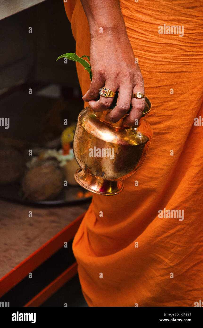 Prêtre en tenant un dhoti orange Kalache de cuivre dans la main droite avec puja préparatifs dans l'arrière-plan, Patit Pavan Sri Ram Mandir, Belgavi, Karnat Banque D'Images