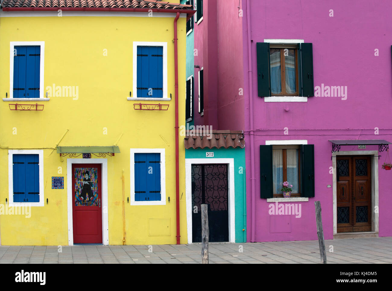 Maisons peintes de couleurs vives en jaune, rose et mauve avec volets rouges à Burano Italie Venise Banque D'Images