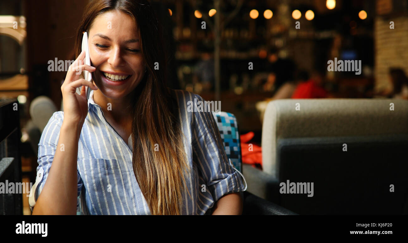 Belle femme assise dans un bar et smiling while holding a phon Banque D'Images