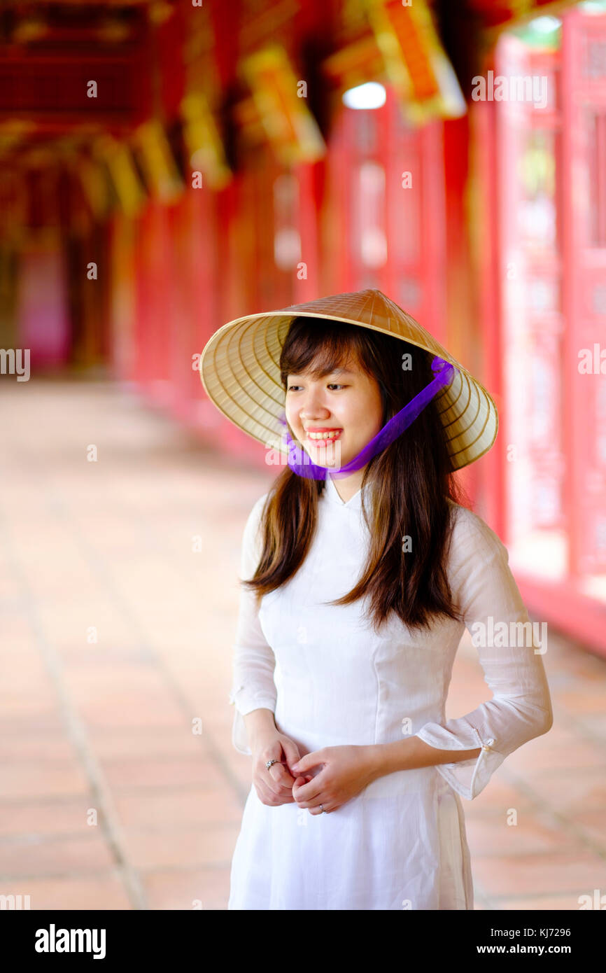 Vietnam, Hue, Cité violette interdite. Jeune femme vietnamienne dans un temple portant une robe Ao Dai traditionnelle et un chapeau conique non asiatique Banque D'Images