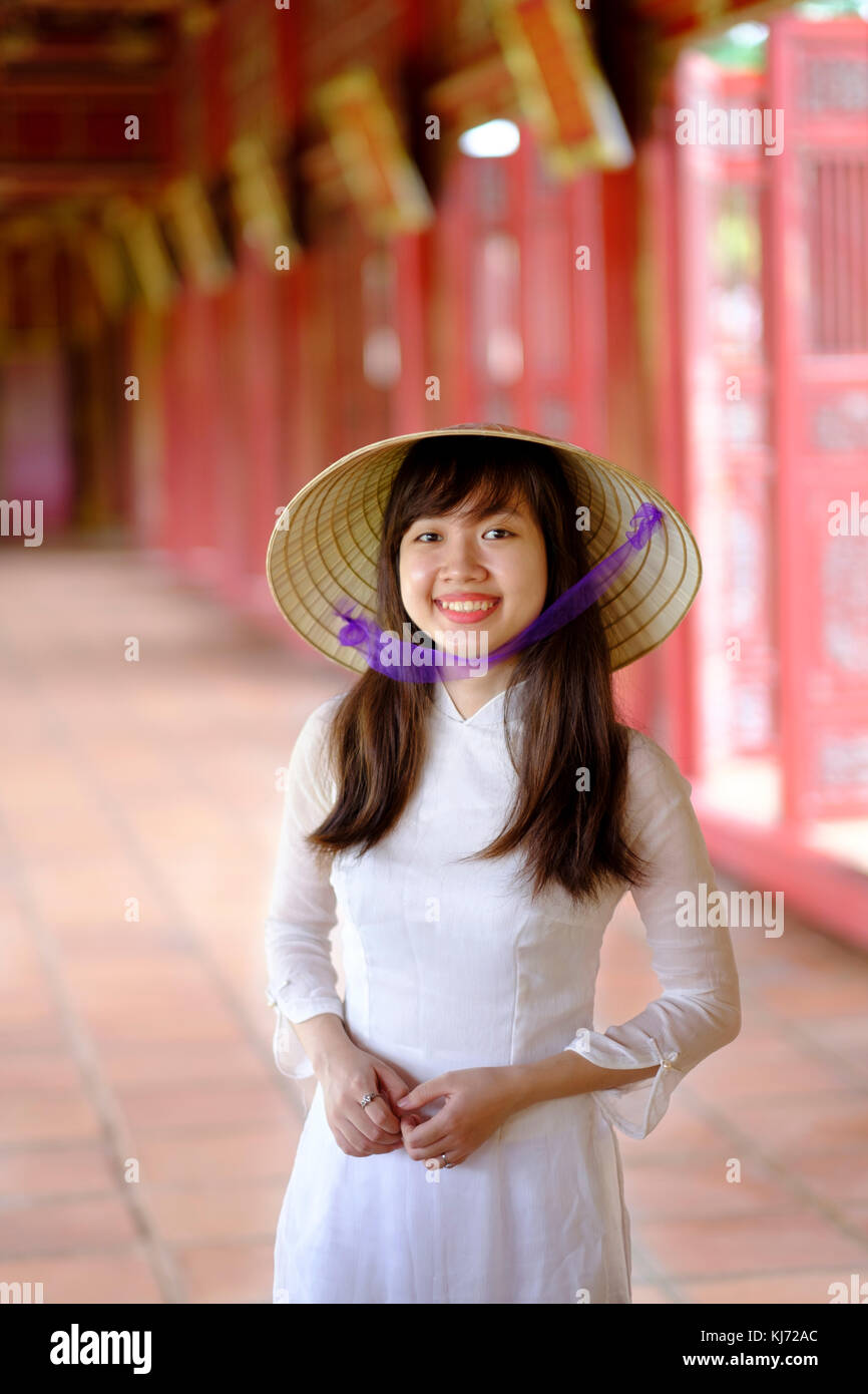 Vietnam, Hue, Cité violette interdite. Jeune femme vietnamienne dans un temple portant une robe Ao Dai traditionnelle et un chapeau conique non asiatique Banque D'Images