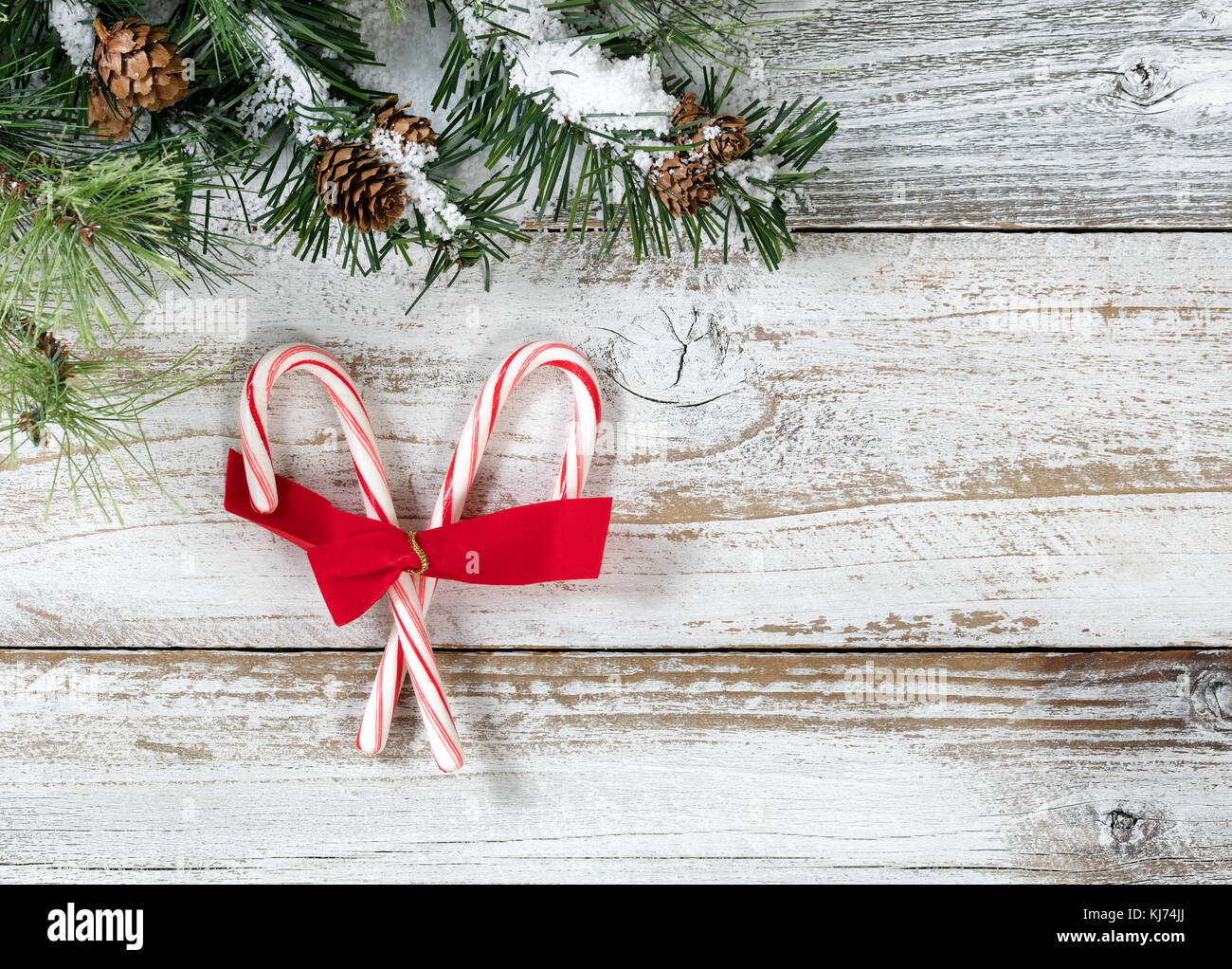Des cannes de Noël et l'arc avec des branches de sapin sur fond de bois blanc rustique Banque D'Images