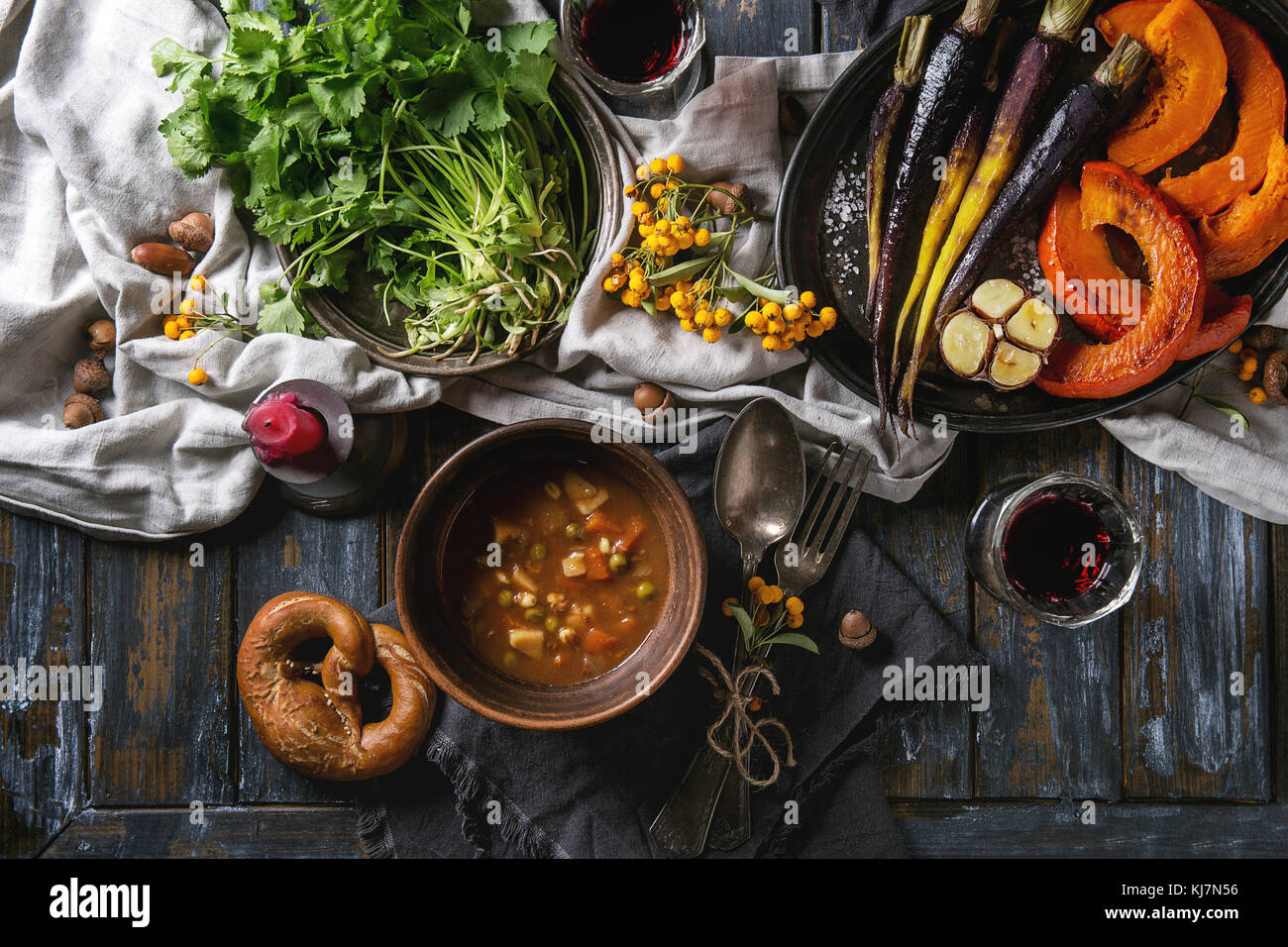 Maison de vacances avec décoration de table bols de soupe chaude, la citrouille, la carotte, l'ail, coriandre fraîche, les bretzels pain, vin rouge, fruits rouges et bougies Banque D'Images