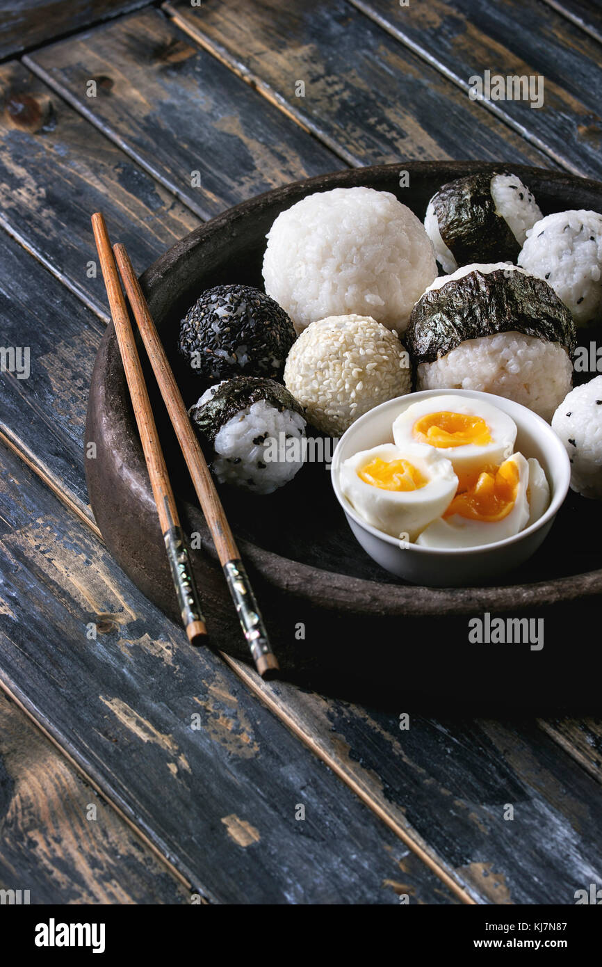 Bac en pierre de taille différente avec des boules de riz et sésame noir Algues Nori, servi avec des œufs durs et baguettes sur planche en bois historique Banque D'Images