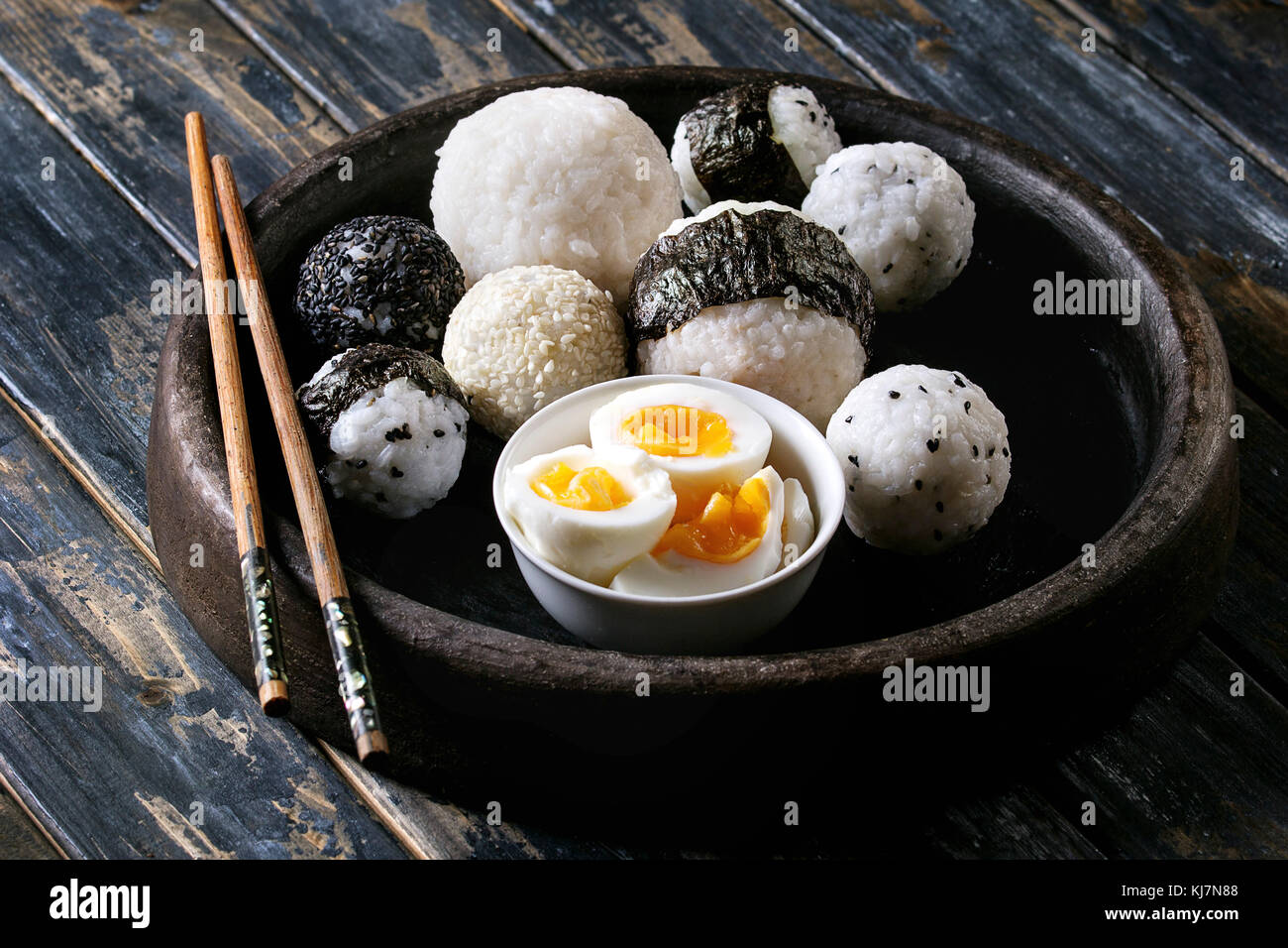 Bac en pierre de taille différente avec des boules de riz et sésame noir Algues Nori, servi avec des œufs durs et baguettes sur planche en bois historique Banque D'Images