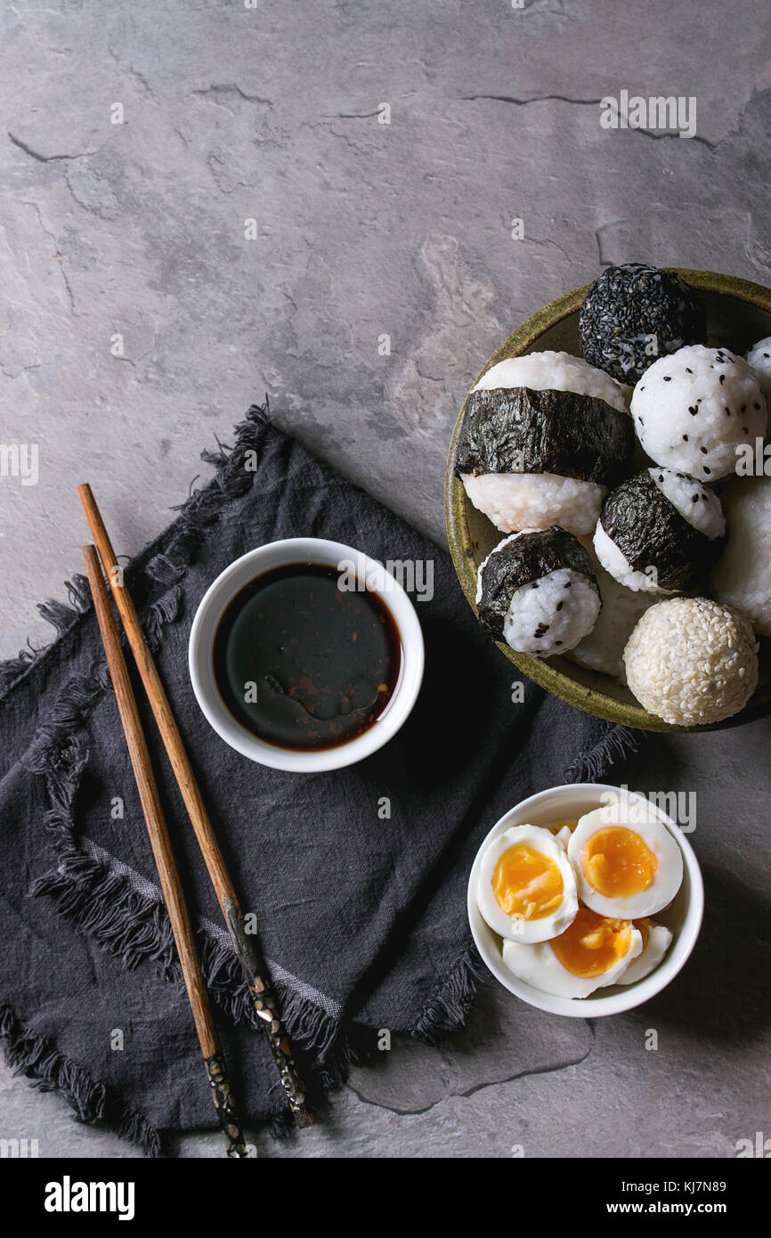 Bol avec différentes tailles de boules de riz et sésame noir avec des Algues Nori, servi avec des œufs durs, de la sauce de soja, des baguettes sur le tableau gris. Asian sty Banque D'Images