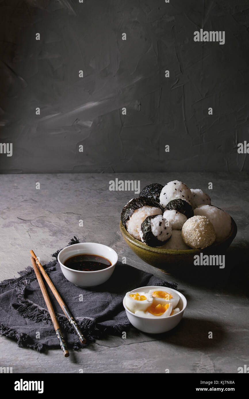 Bol avec différentes tailles de boules de riz et sésame noir avec des Algues Nori, servi avec des œufs durs, de la sauce de soja, des baguettes sur le tableau gris. Asian sty Banque D'Images
