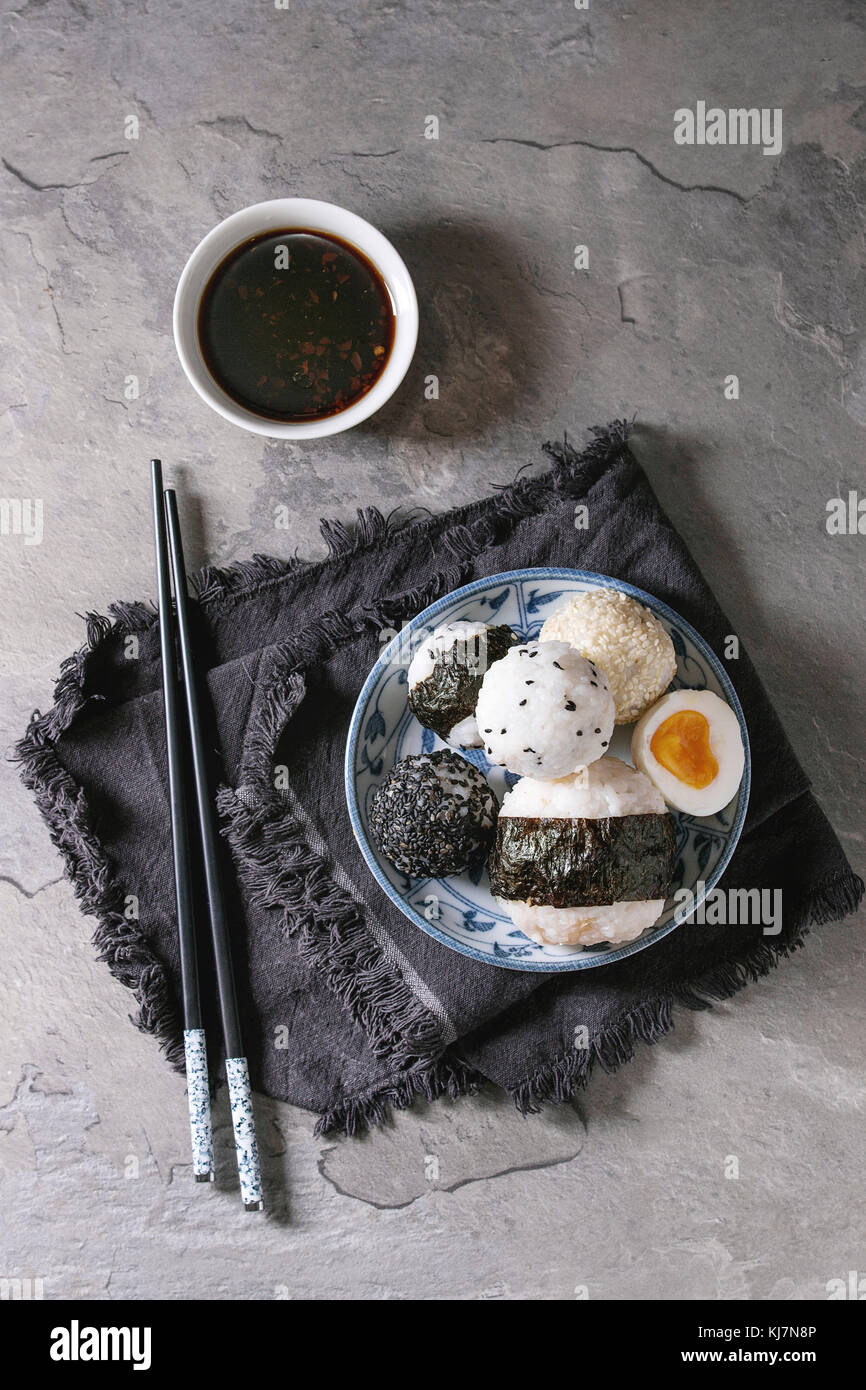 Plaque bleue avec différentes tailles de boules de riz et sésame noir avec des Algues Nori, servi avec des œufs durs, de la sauce de soja, des baguettes sur le tableau gris. Asi Banque D'Images