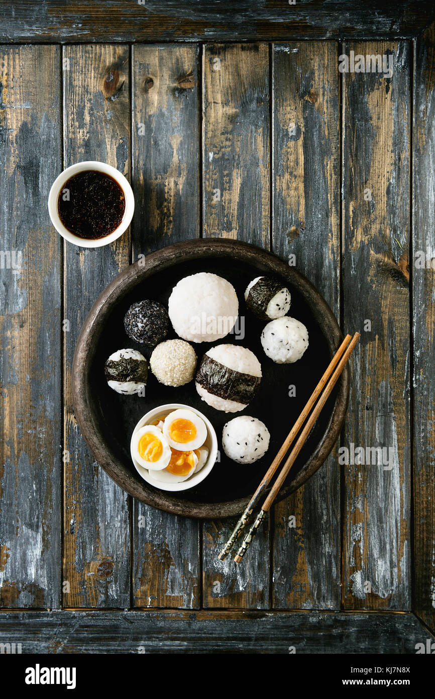 Bac en pierre de taille différente avec des boules de riz et sésame noir Algues Nori, servi avec des œufs durs, de la sauce de soja, baguettes sur planche en bois ba Banque D'Images