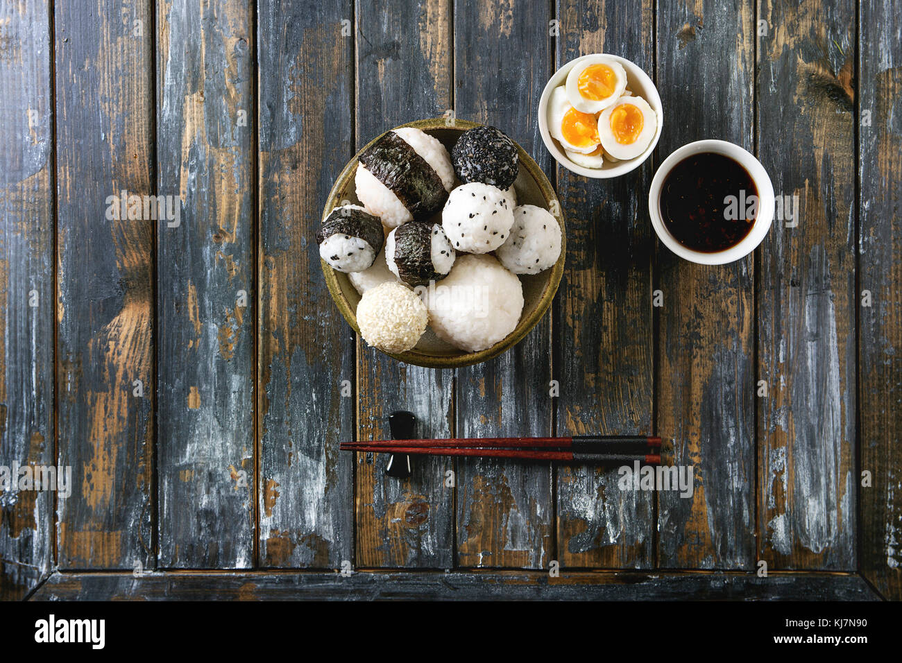 Bac en pierre de taille différente avec des boules de riz et sésame noir Algues Nori, servi avec des œufs durs, de la sauce de soja, baguettes sur planche en bois ba Banque D'Images