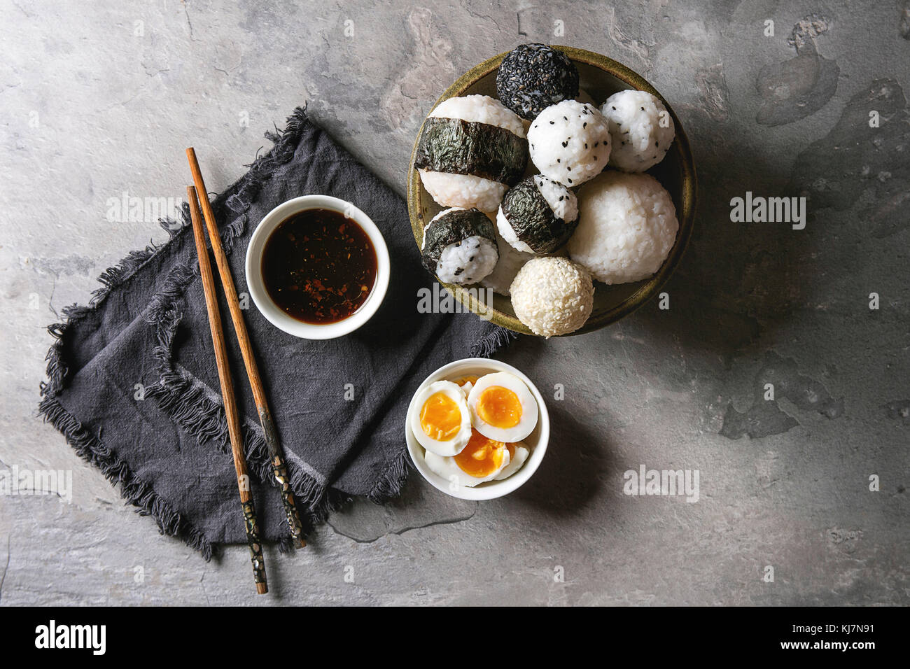 Bol avec différentes tailles de boules de riz et sésame noir avec des Algues Nori, servi avec des œufs durs, de la sauce de soja, des baguettes sur le tableau gris. Asian sty Banque D'Images
