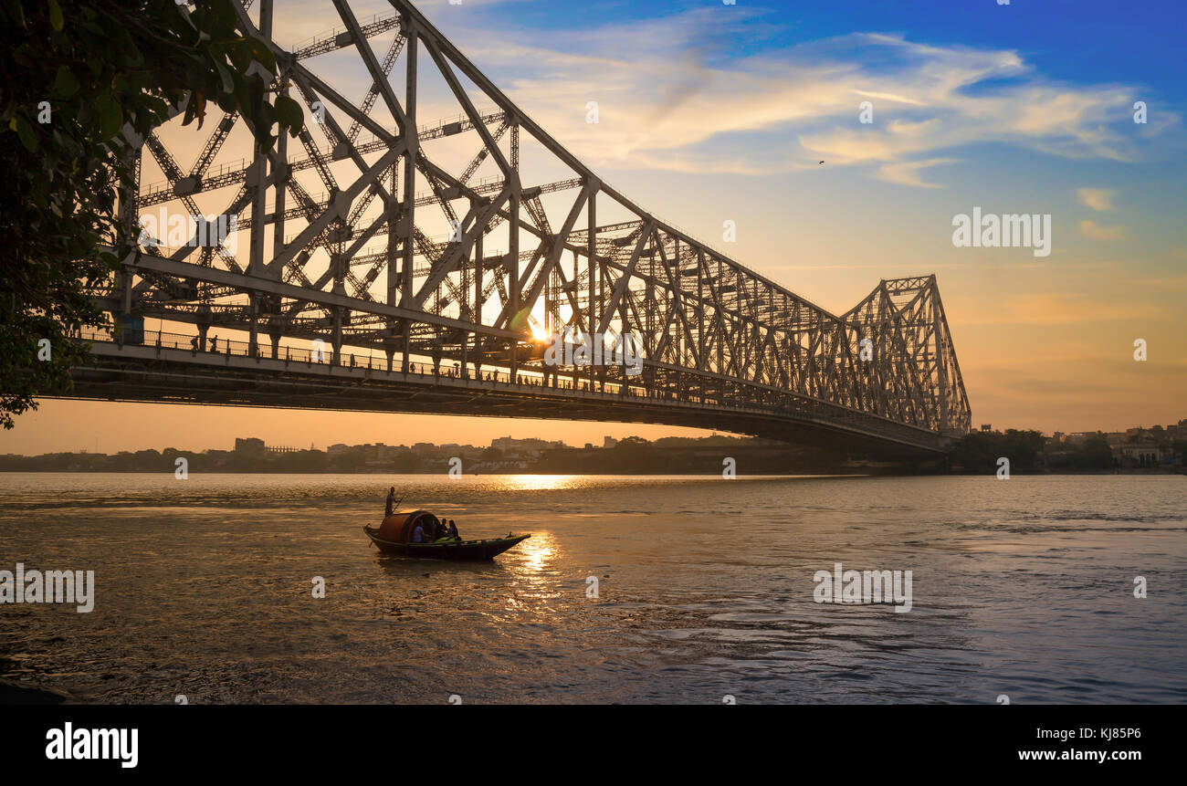 Howrah Bridge au lever du soleil avec moody sky et bateau en bois sur la rivière Hooghly. Banque D'Images