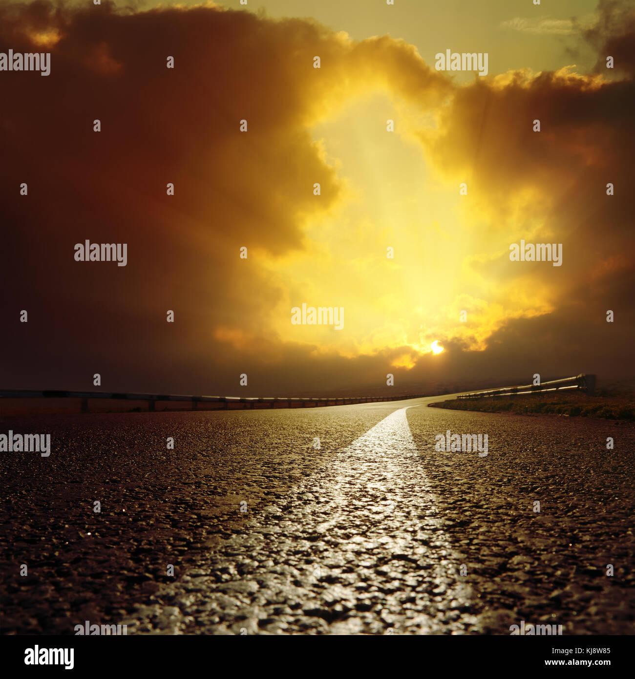 Route asphaltée va à la lumière du coucher du soleil dans les nuages. Banque D'Images