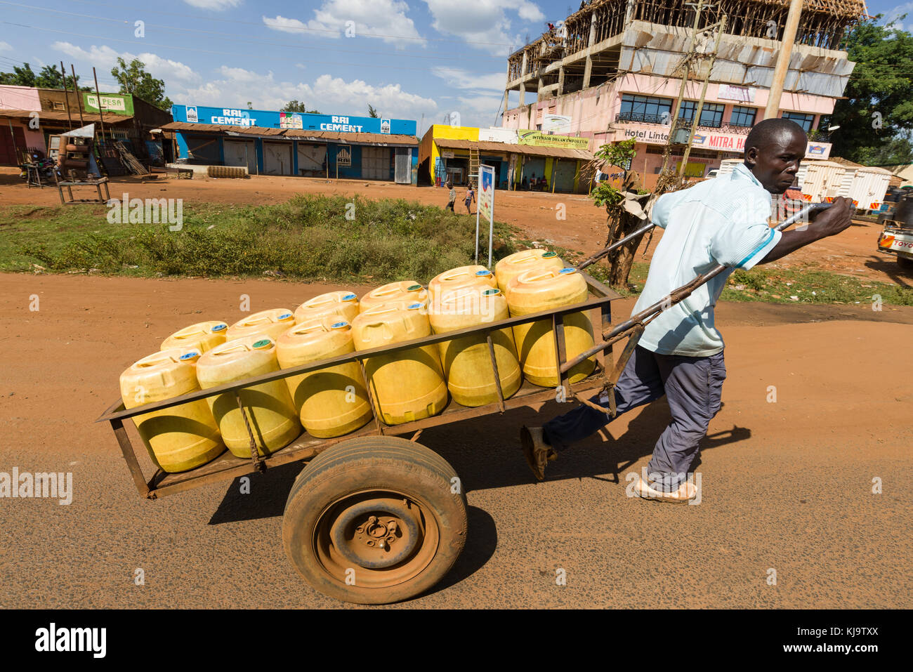 Un homme tire une charrette chargée de bidons d'eau en plastique jaune sur la route grâce à une petite ville, Kenya, Afrique de l'Est Banque D'Images