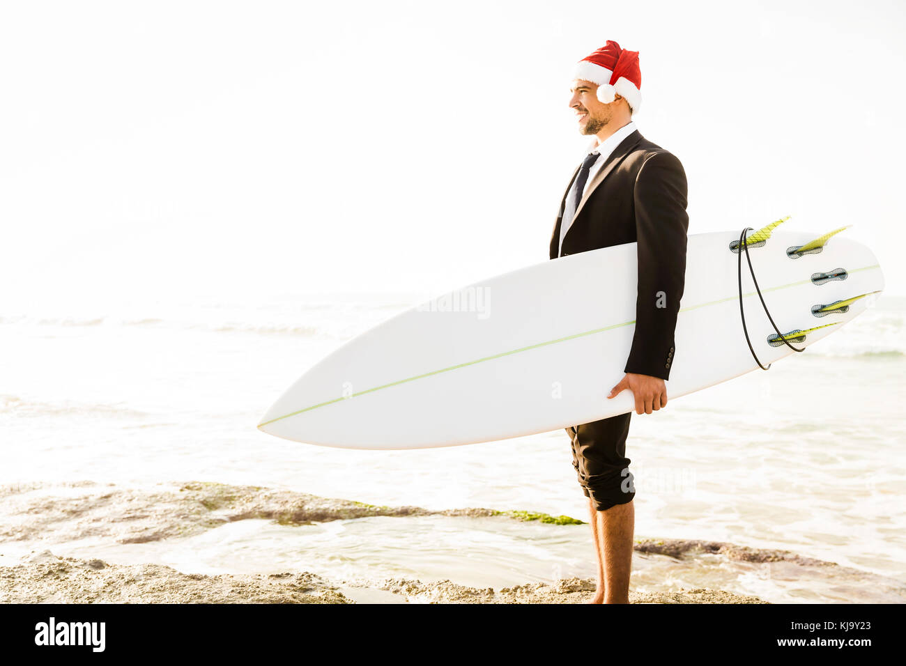 Surfeur d'affaires wearing a Santa hat and holding a surfboard Banque D'Images