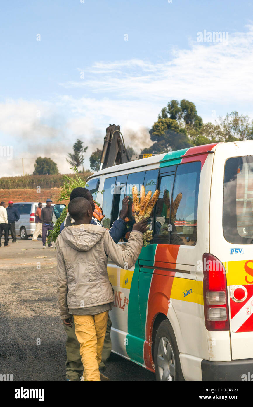 African Male camelots essaient de vendre le maïs cuit à passagers dans un minibus par la route de matatu, Kenya, Afrique de l'Est Banque D'Images