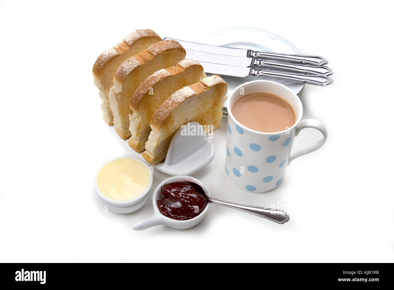 Toast blanc en tranches de pain grillé avec du beurre en rack en céramique rouge, confiture, tasse de thé et les assiettes et les couteaux sur fond blanc. Banque D'Images