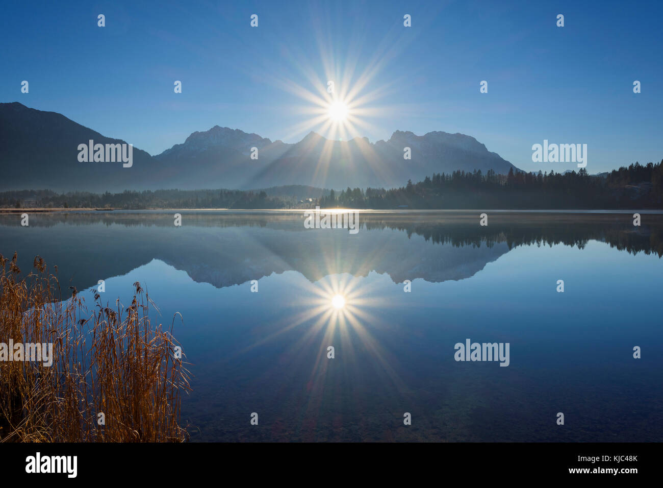 Les montagnes Karwendel sont rétroéclairées contre le soleil éclatant qui se reflète dans le lac Barmsee à Kruen, en haute-Bavière, en Allemagne Banque D'Images