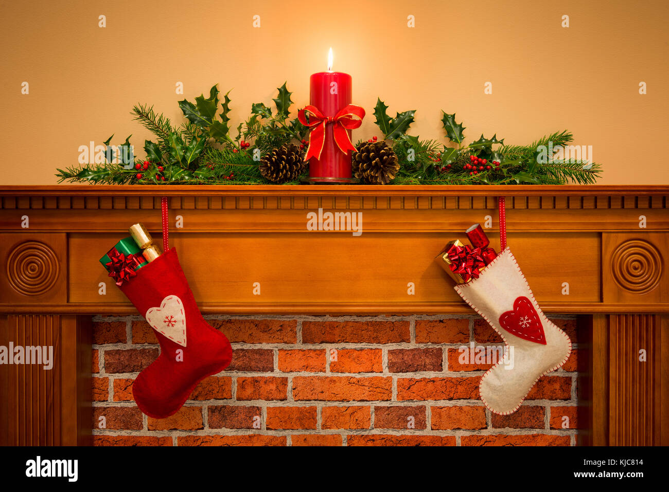 Deux bas de Noël avec gift wrapped présente suspendu par une cheminée sur une cheminée, plus que les bougies de fête avec garland y compris holly Banque D'Images