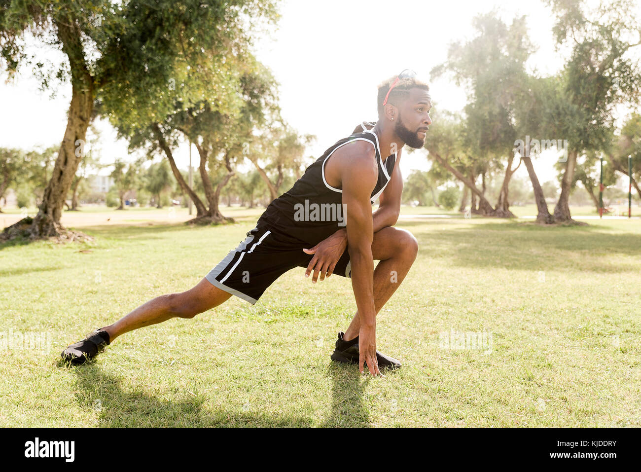 Black man crouching in park qui s'étend les jambes Banque D'Images