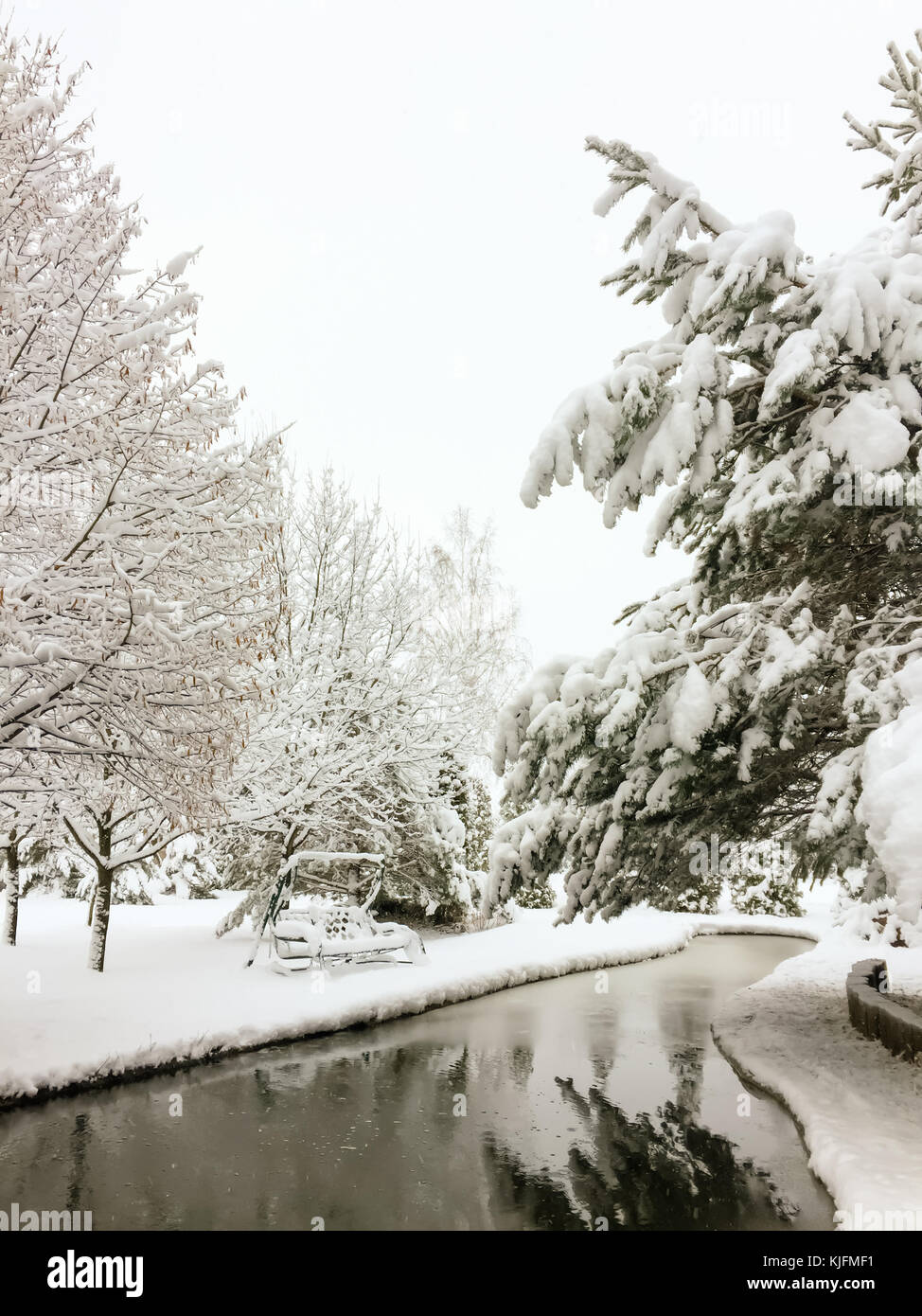 Paysage d'hiver magique dans un parc avec un étang et balançoires de jardin couvert de la première neige pelucheuse. Banque D'Images