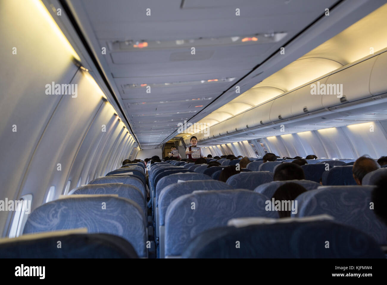 La cabine d'un avion avec Airhostess disant avis de sécurité, comme vu de l'arrière de l'avion Banque D'Images