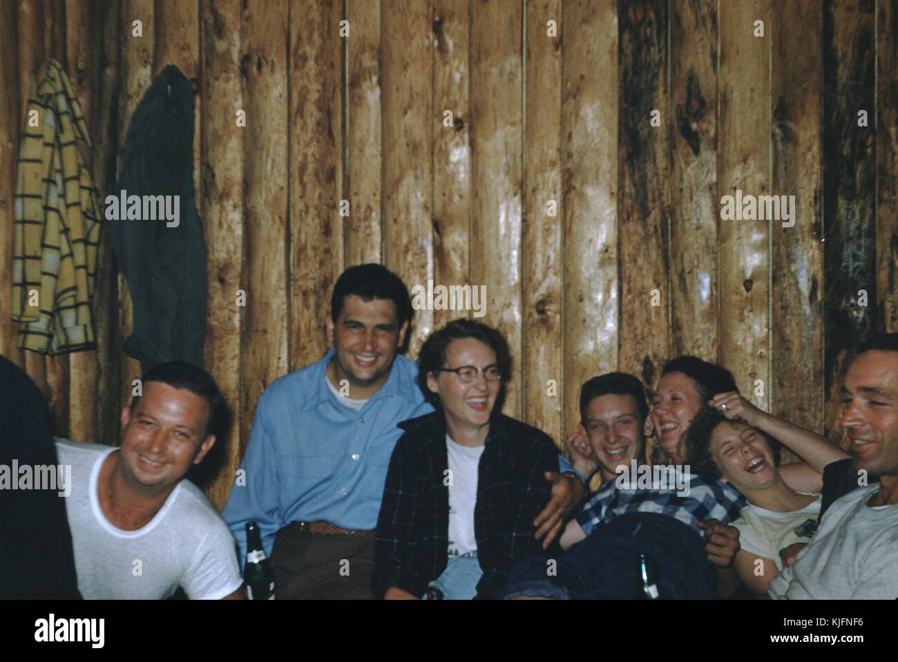 Amis hommes et femmes à une fête, apparemment ivre, boire de la bière, rire, et se câliner ensemble, dans une salle avec un mur de bois, 1948. Banque D'Images