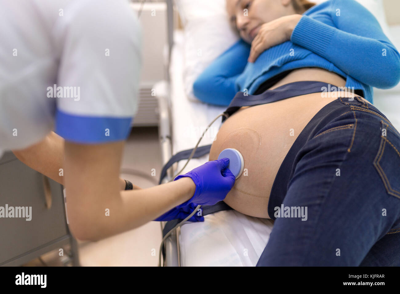 Jeune femme heureuse allongé sur un lit dans un hôpital tout en fixant une cardiotocography médecin d'examiner le capteur de rythme cardiaque du fœtus. Banque D'Images
