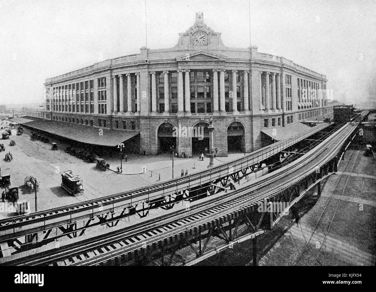 Une photographie extérieure prise d'une élévation de South Station, il a été construit en 1899 pour remplacer plusieurs terminaux de chemin de fer, il sert de centre de transport pour les bus, le métro, Et le train, des voies de train surélevées peuvent être vues en cours de route à côté du bâtiment avec une plate-forme située entre eux, les gens peuvent être vus à l'extérieur du bâtiment avec des voitures tirées par des chevaux et un chariot, Boston, Massachusetts, 1905. Banque D'Images