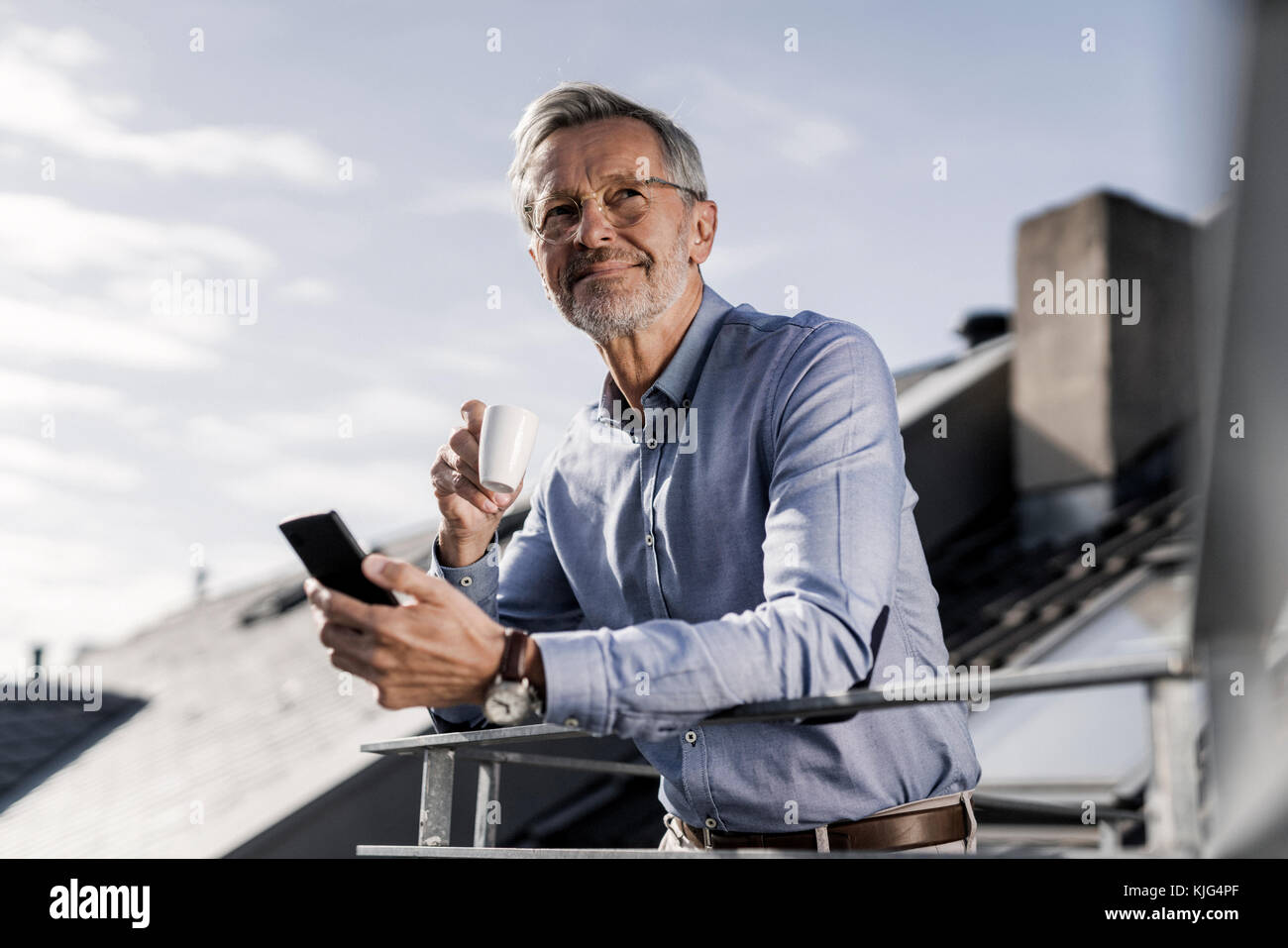 Homme aux cheveux gris avec debout sur smartphone balkony boire du café Banque D'Images Homme aux cheveux gris avec debout sur smartphone balkony boire du café Banque D'Images