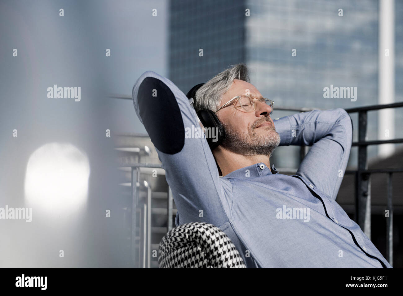Homme aux cheveux gris relaxing in chair sur le balcon d'écouter de la musique Banque D'Images
